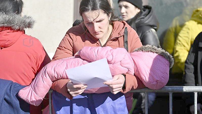 Menschen wartet mit einem Kind im Arm vor einem Zentrum zur Registrierung und Unterbringung von Geflüchteten in Brüssel. Foto: Eric Lalmand/BELGA/dpa