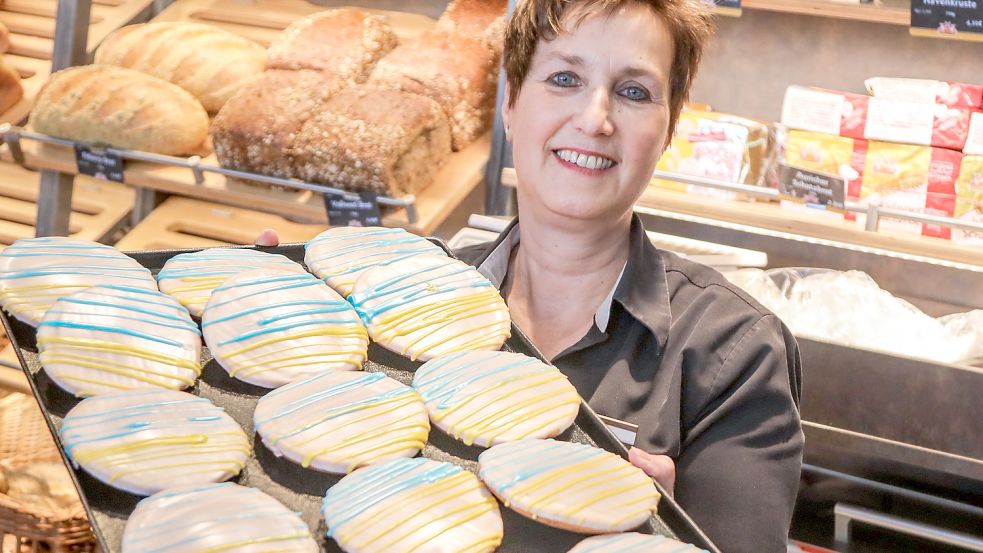 Dagmar Janssen (Filialleiterin der Wikingerbäckerei in Aurich) hält ein Blech mit Amerikanern. Die Gebäckstücke sind in den Farben der ukrainischen Nationalflagge verziert. Foto: Romuald Banik