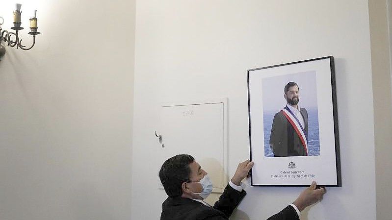 Ein Palastangestellter hängt das offizielle Porträt des neuen chilenischen Präsidenten Boric im Büro des Präsidentenpalastes La Moneda auf. Foto: Matias Delacroix/AP/dpa