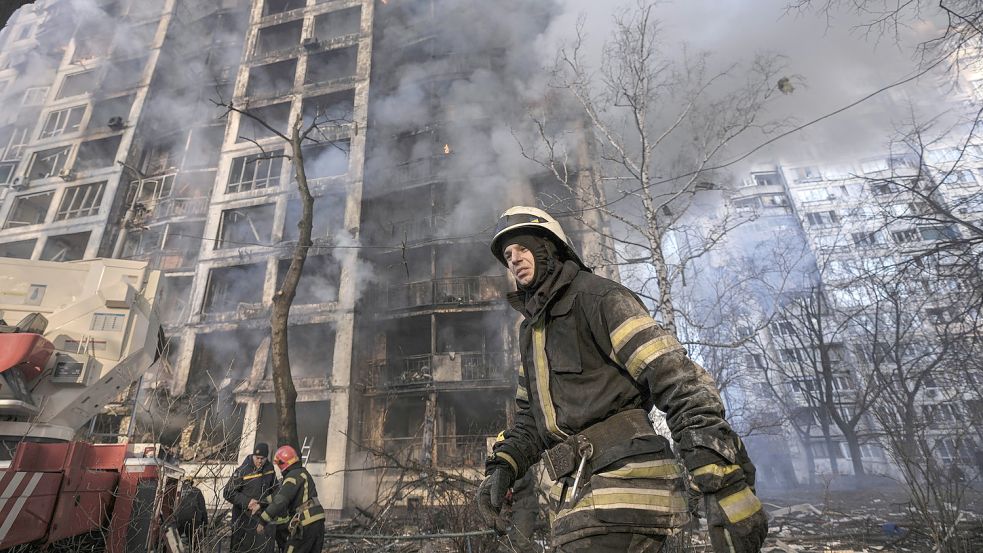 Einsatzkräfte der Feuerwehr stehen in der Ukraine vor einem brennenden Wohngebäude, das durch Bombenbeschuss des russischen Militärs zerstört wurde. Foto: DPA