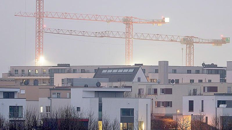Kräne auf einer Baustelle für Wohnungen stehen hinter Mehrfamilienhäusern des relativ neuen Stadtteils Kalbach-Riedberg in Frankfurt. Foto: Sebastian Gollnow/dpa