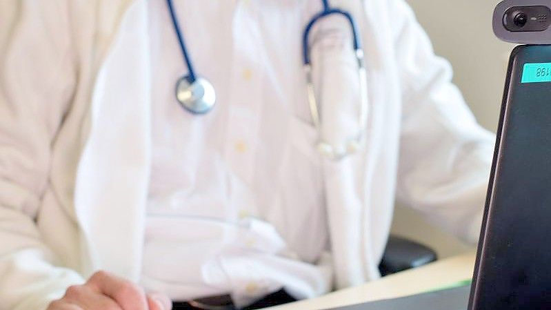 Ein Hausarzt sitzt während einer Videosprechstunde in seiner Praxis vor einem Laptop. Foto: Monika Skolimowska/ZB/dpa