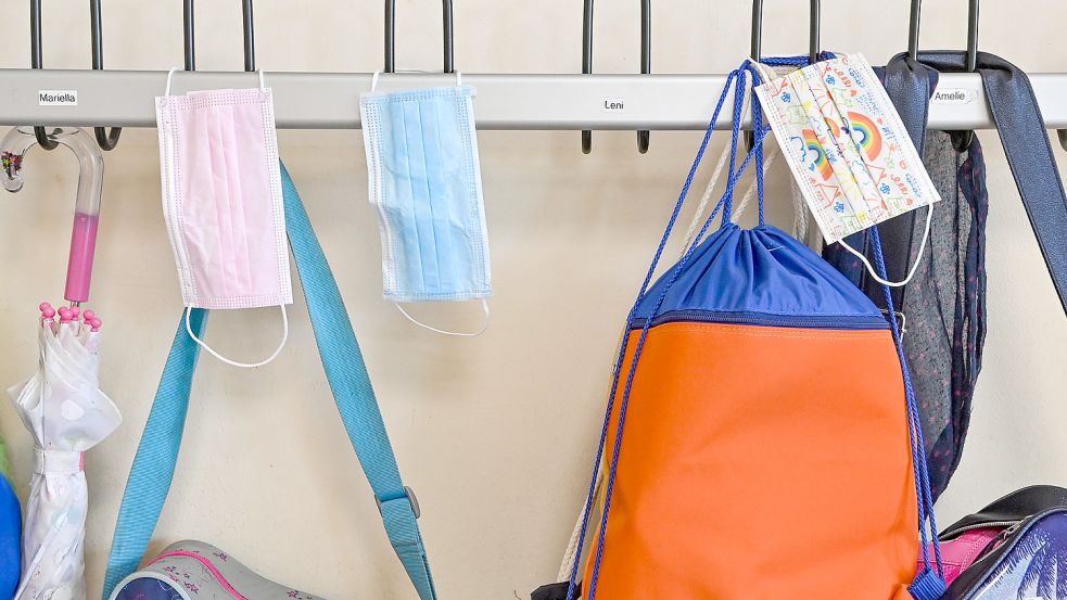 Masken hängen an Kleiderhaken in einer Grundschule. Nicht in allen Einrichtungen im Kreis muss sie am Platz noch getragen werden. Foto: DPA