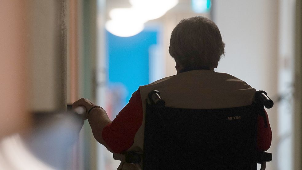 Eine Frau sitzt in einem Pflegeheim in einem Rollstuhl auf einem Gang. Foto: DPA