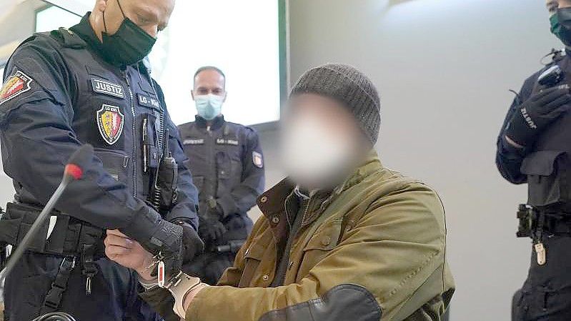 Ein Justizbeamter entfernt die Handschellen des Angeklagten (2.v.r) im Sitzungssaal des Landgerichts Kiel. Foto: Marcus Brandt/dpa