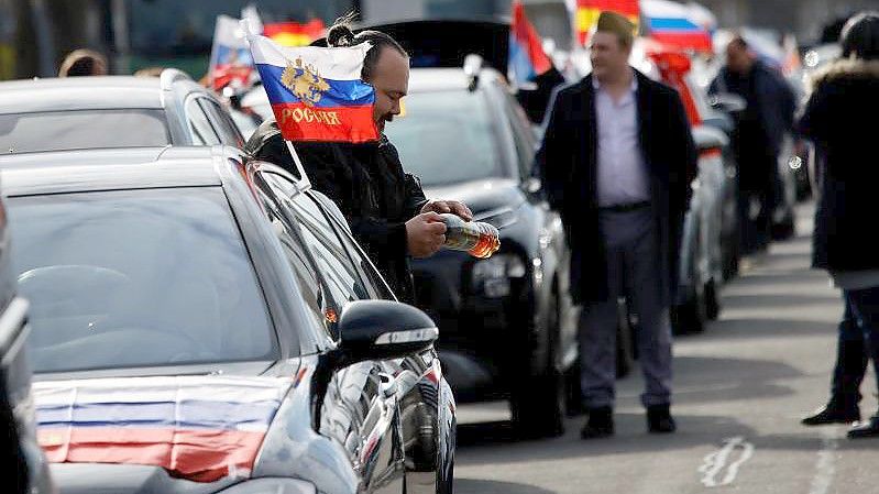 Flaggen mit den russischen Nationalfarben und dem russischen Staatswappen wehen an einem Auto auf dem Olympiaplatz vor dem Olympiastadion. Foto: Carsten Koall/dpa