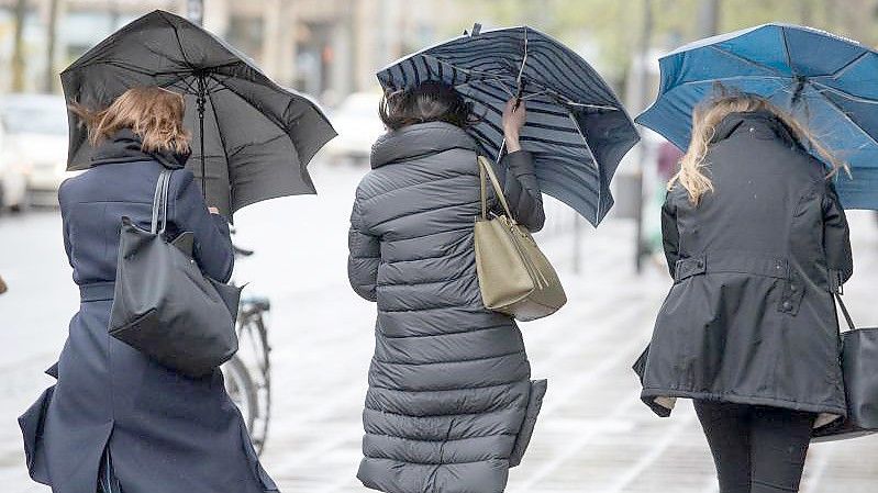 Eine Sturmböe erfasst die Regenschirme von drei Frauen in Frankfurt. Foto: Boris Roessler/dpa