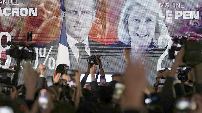 Ein Bildschirm in Paris zeigt den französischen Präsidenten Macron und die rechtsextreme Kandidatin Le Pen am Wahltag. Die beiden kämpfen in einer Stichwahl am 24. April um das höchste Amt im Land. Foto: Francois Mori/AP/dpa