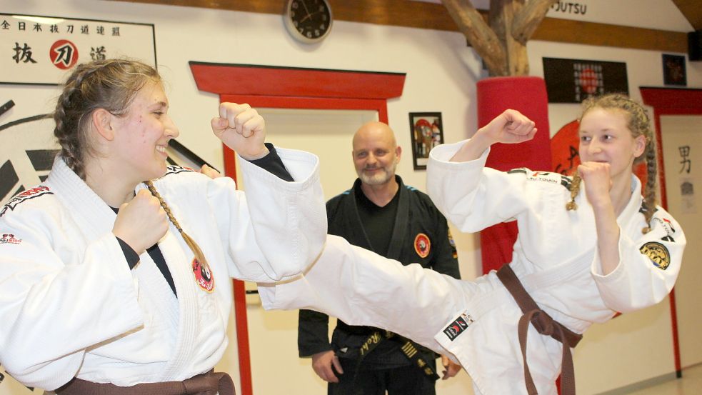 Meisterschülerin Amelie Weigl (rechts) demonstriert einen Tritt gegen die Schulter ihrer Trainingspartnerin Marie Birkel. Ju-Jutsu-Lehrer Sven Rohl (5. Dan) beobachtet das Geschehen auf der Matte im Übungsraum, auch Dojo genannt, des TuS Aurich-Ost in Wallinghausen. Fotos: Wolf-Rüdiger Saathoff