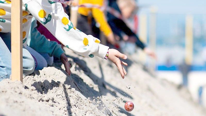 Kinder lassen am Ostersonntag bunte Eier von einer aufgeschütteten Düne am Weststrand von Norderney heruntertrullern. Foto: Hauke-Christian Dittrich/dpa