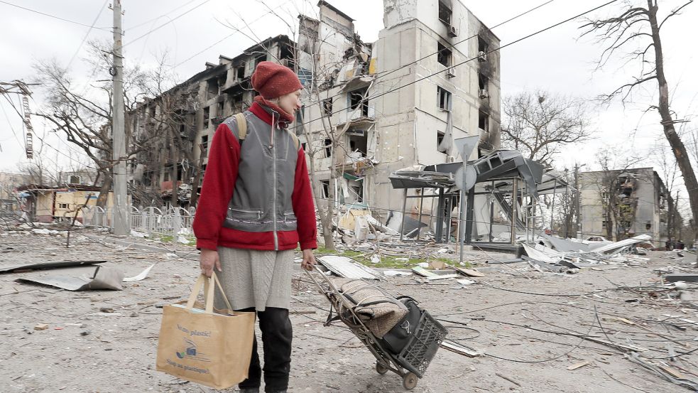 Eine Anwohnerin mit Gepäck vor einem zerstörten Wohnhaus in Mariupol. Foto: dpa/Xinhua