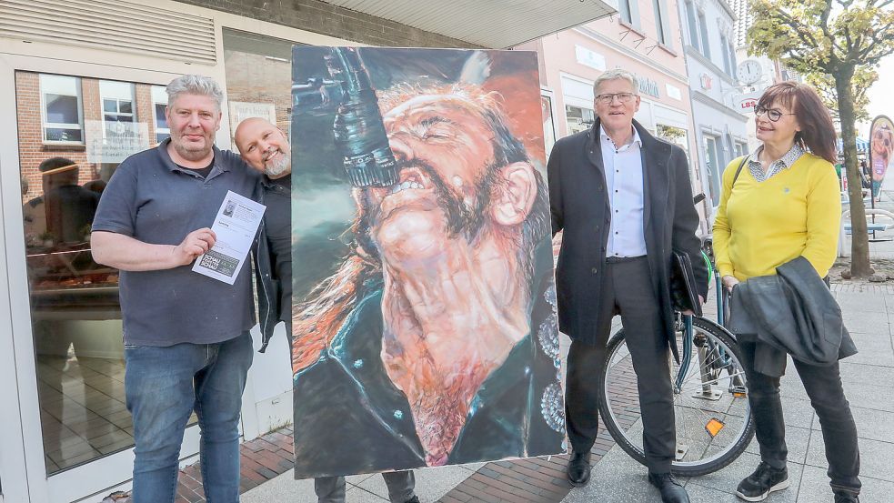 Metzger Volker Lambrecht (von links), zweiter Vorsitzender des Kunstvereins Nicolaus Hippen, Auricher Bürgermeister Horst Feddermann und Sabine Klotter vom Kunstverein Aurich präsentieren eines der Werke. Es hängt im Schaufenster der Metzgerei Wilhelm Lambrecht in der Norderstraße in Aurich. Foto: Romuald Banik