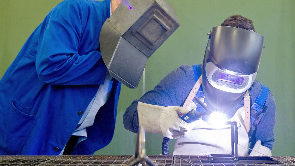 Ein Auszubildender (r) setzt eine Schweißnaht an ein Metallteil, während ein Berufsschullehrer zuschaut. Die Zahl der Lehrverträge im Elektro- und Metallhandwerk in Ostfriesland ist gesunken. Foto: DPA