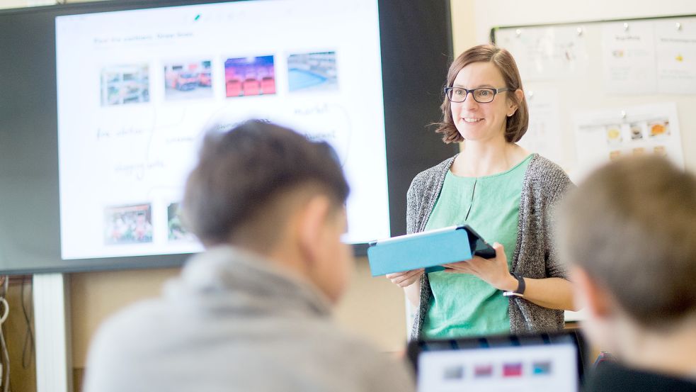 Eine Lehrerin steht mit einem iPad vor einer digitalen Schultafel. Foto: dpa/Julian Stratenschulte