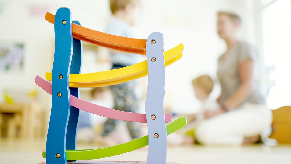 Eine Erzieherin spielt in einer Kindertagesstätte hinter einer Rollbahn mit Kindern. Foto: DPA