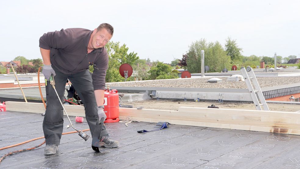 Dachdeckermeister Dennis Cramer trägt auf einem Flachdach die erste Dampfsperre auf. Foto: HWK