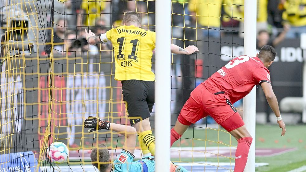 Dortmunds Marco Reus (M) stochert den Ball gegen Leverkusens Torwart Lukas Hradecky (l) und Piero Hincapie über die Linie. Foto: Bernd Thissen/dpa