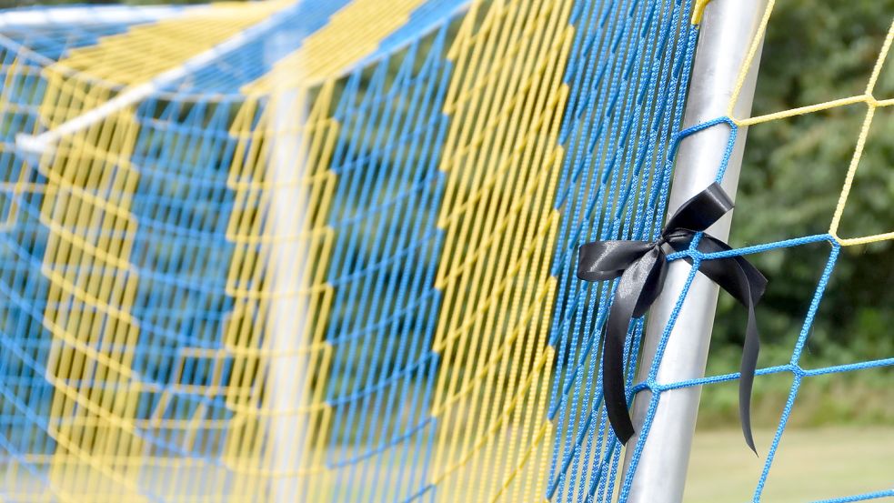 Ein Trauerflor hängt auf dem Sportplatz in Upgant-Schott an einem Tor mit Maschen in den gelb-blauen Vereinsfarben des FC Brookmerland. Foto: Thomas Dirks