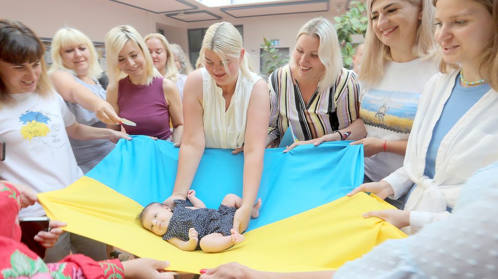 Maria Al-Battat legt ihre Tochter Adelina auf eine ukrainische Fahne, die von aus der Ukraine geflüchteten Frauen gehalten wird. Maria Al-Battat war auf der Flucht aus ihrer Heimat schwanger, Adelina wurde in Aurich geboren. Foto: Romuald Banik