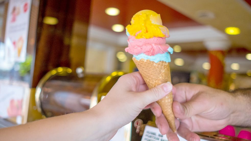 ine Frau kauft bei sonnigem Wetter drei Kugeln Eis in einer Waffel. Foto: DPA
