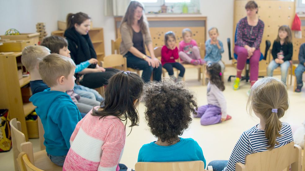 Kinder und Erzieherinnen sitzen in einer Kindertagesstätte in Düsseldorf im Kreis. Foto: DPA