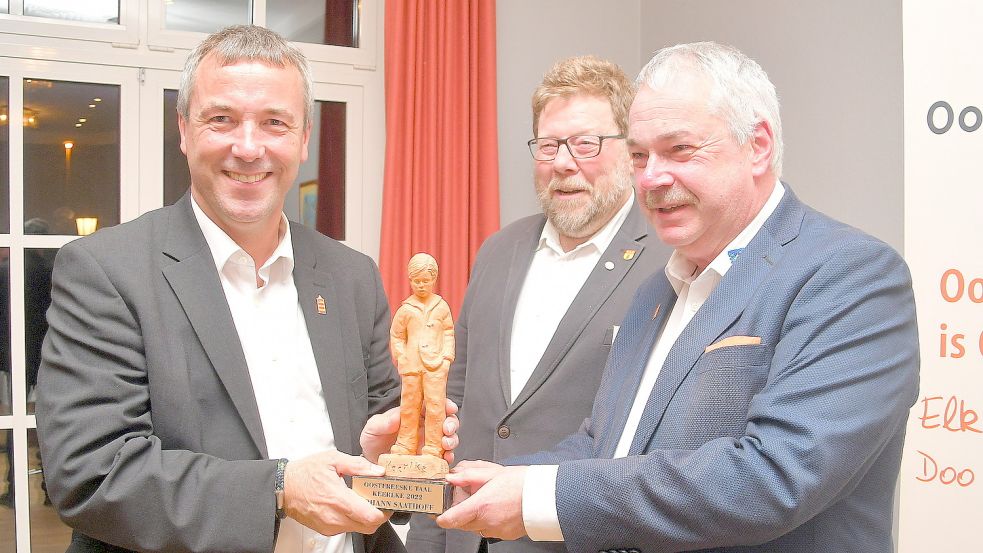 Johann Saathoff (links) erhält aus der Hand seines Freundes Frank Baumann, der eine wunderbare humorige Laudatio auf Johann Saathoff hielt, den „Keerlke“. Hinter ihnen Hans Freese, Vorsitzender von Oostfreeske Taal. Foto: Gerd-Arnold Ubben