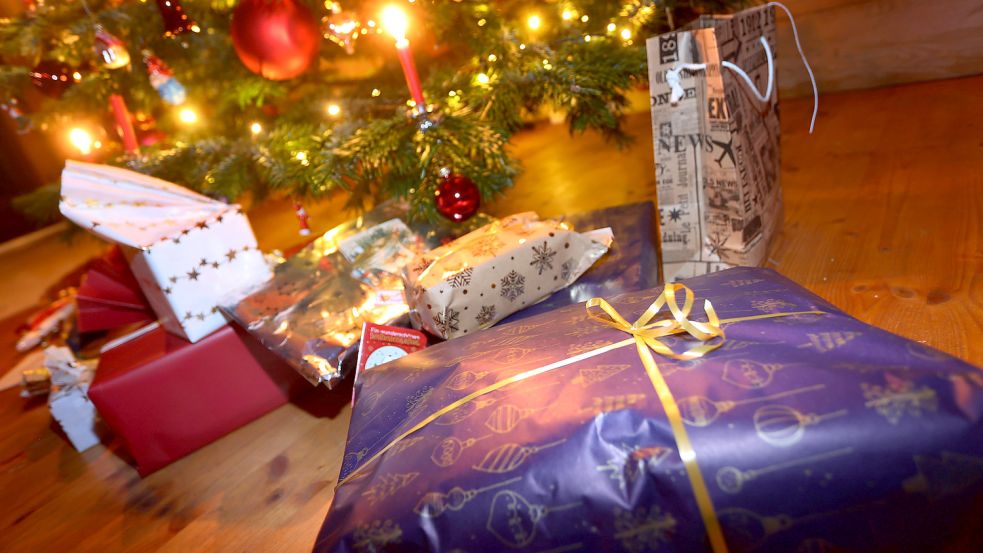 Verpackte Geschenke liegen in einem Wohnzimmer unter einem festlich geschmücktem Weihnachtsbaum. Foto: DPA