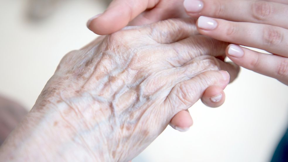 Eine Frau streichelt die Hand einer Seniorin. Foto: DPA
