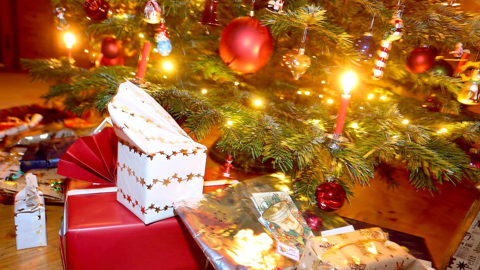 Verpackte Geschenke liegen in einem Wohnzimmer unter einem festlich geschmücktem Weihnachtsbaum. Foto: DPA
