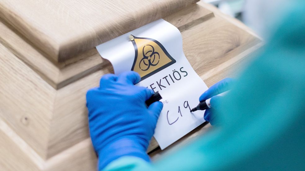 Ein Bestattungsunternehmer schreibt „C19“ auf ein Schild mit dem Hinweis „Infektiös“ auf einen Sarg mit einem Verstorbenen, der an dem Coronavirus gestorben ist. Foto: Rolf Vennenbernd/dpa