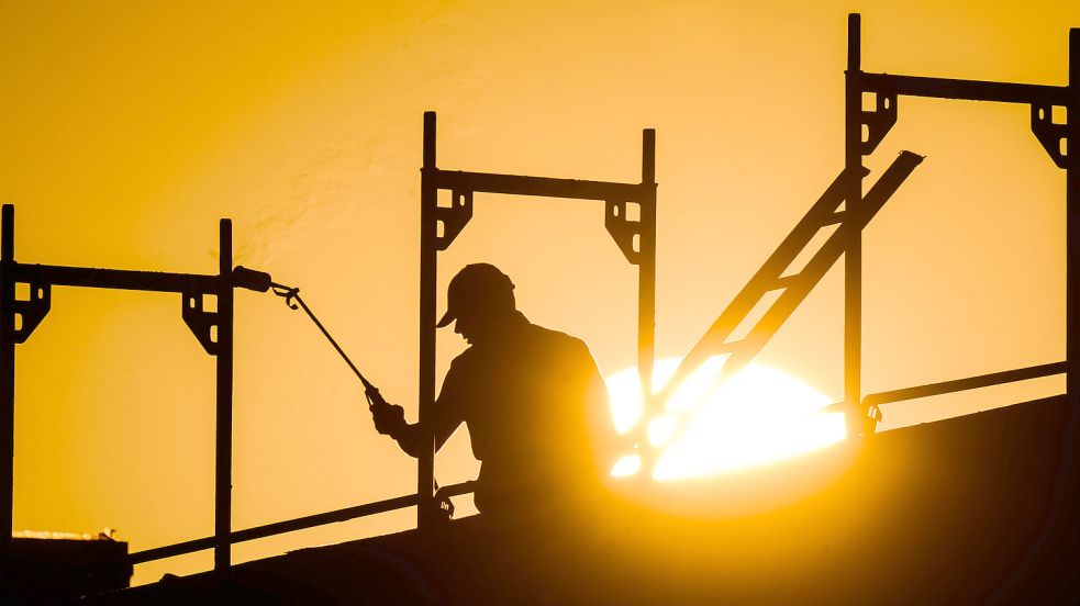 Ein Bauarbeiter steht mit einem Gasbrenner beim Bau eines Mehrfamilienhauses, als am Horizont die Sonne aufgeht. Foto: DPA