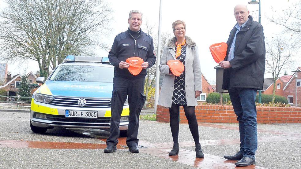 Uwe Schwarz von der Polizeistation Großefehn (von links), die Großefehntjer Gleichstellungsbeauftragte Sonja Alberts und Bürgermeister Erwin Adams präsentieren die orangefarbigen Sattelkissen, die zum Aktionstag verteilt wurden. Foto: privat