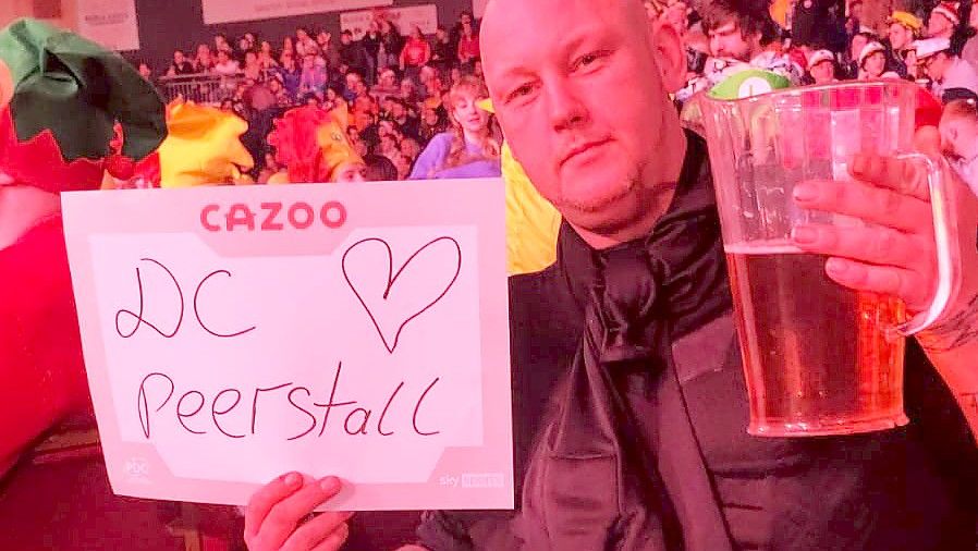 Ralf Rose macht im Londoner Alexandra Palace auf den Dart-Club Peerstall aus Moordorf aufmerksam und hält einen Pitcher Bier in der Hand.