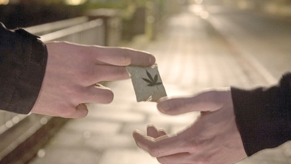 Die gestellte Szene zeigt zwei Männer bei der Übergabe eines Tütchen Marihuanas auf einer Straße. Foto: DPA