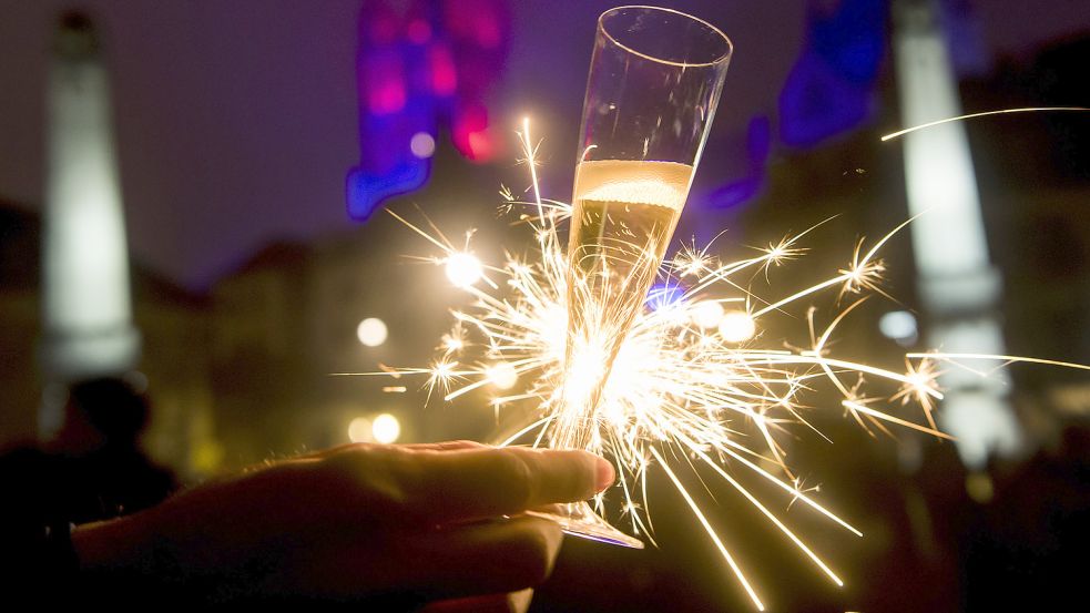 Eine Frau hält ein Glas Sekt und eine Wunderkerze in der Hand. Foto: DPA