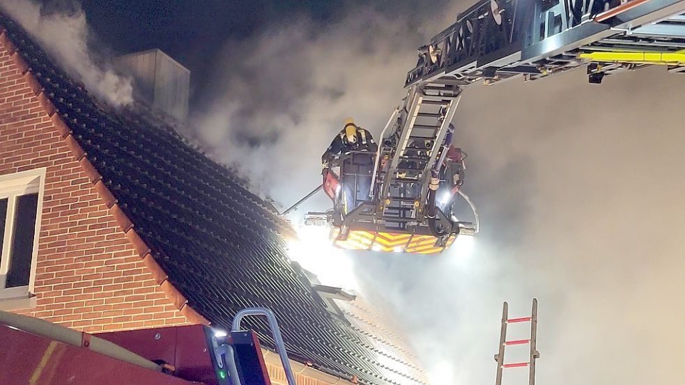 Feuerwehrleute entfernten Dachziegel bei dem Wohnhaus in Hage, um die Flammen zu bekämpfen. Foto: Rebecca Kresse