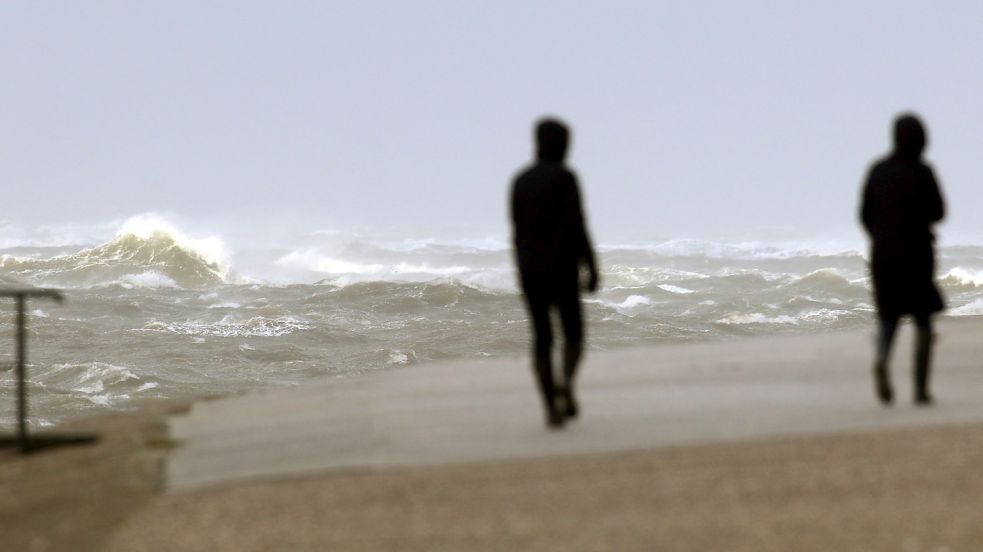 Spaziergänger gehen an der aufgepeitschten Nordsee entlang. Foto: DPA