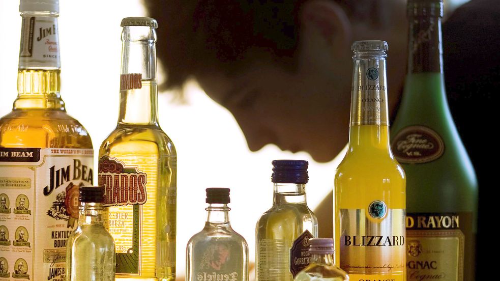 Ein Jugendlicher sitzt hinter Flaschen mit Schnaps und anderen alkoholischen Getränken. Der Verkauf von hochprozentigem Alkohol an Minderjährige ist in Deutschland verboten. Foto: DPA