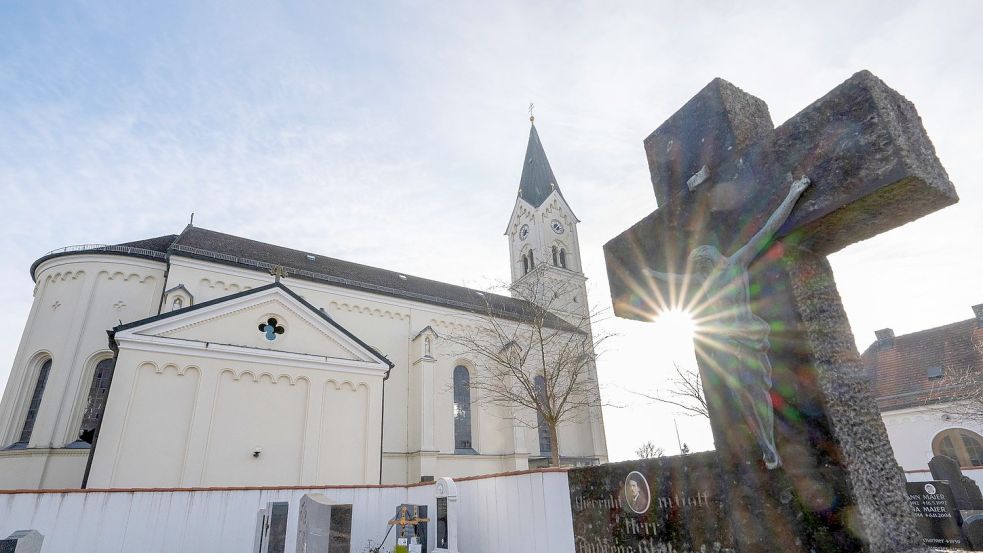 Das Kreuz eines Grabsteins steht vor der katholische Kirche St. Nikolaus in Garching. Foto: Peter Kneffel/dpa