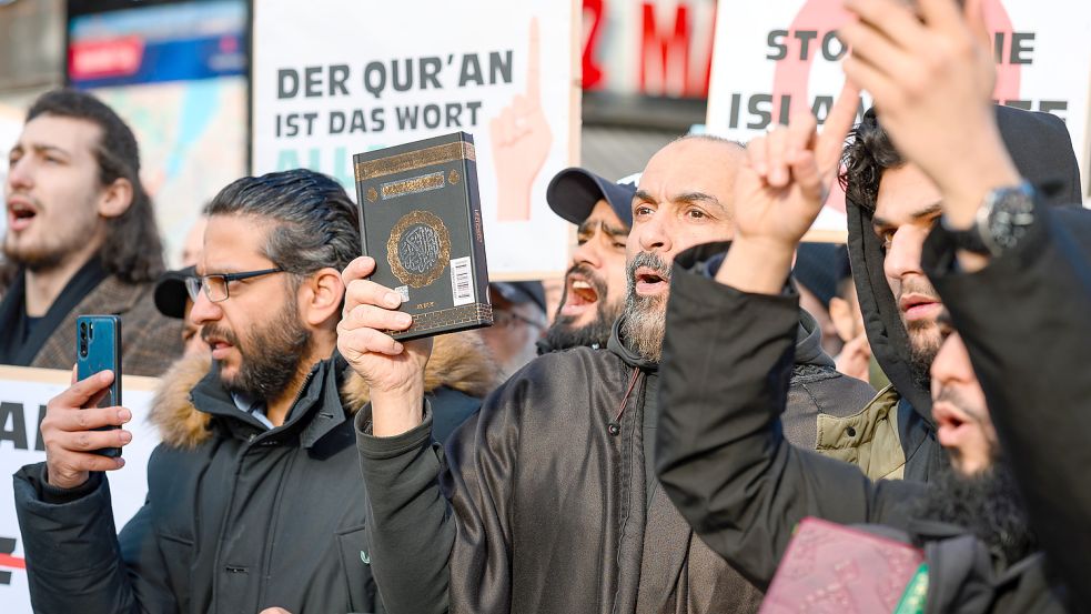 Demonstrationsteilnehmer halten den Koran in die Höhe. Bei einer Kundgebung gegen eine Koranverbrennung in Schweden sind in Hamburg mehrere tausend Menschen auf die Straße gegangen. Die Demonstration war von Islamisten organisiert worden. Foto: dpa/Jonas Walzberg