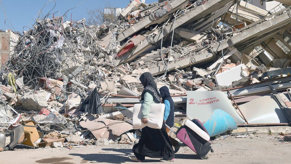 Menschen gehen nach den verheerenden Erdbeben an einem eingestürzten Gebäude in der türkischen Stadt Adiyaman vorbei. Foto: DPA