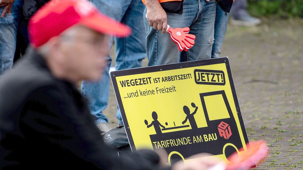 „Wegezeit ist Arbeitszeit!“ steht auf dem Plakat eines Teilnehmers einer Kundgebung der IG Bau im Sommer 2021. Inzwischen soll die vereinbarte Entschädigung ausgezahlt werden. Foto: DPA