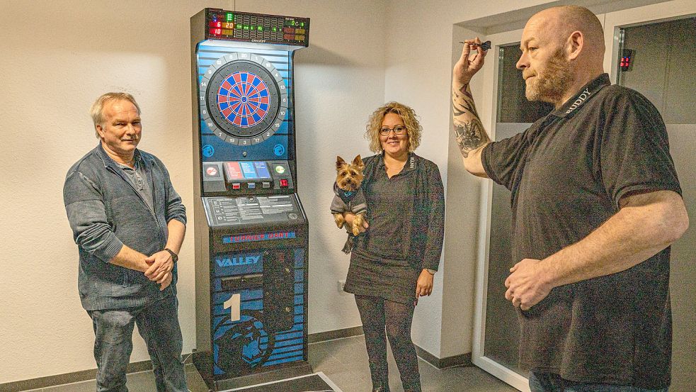 Der Vorsitzende des TV Osteel, Andreas Palluck (links), Antje Leupold (mit Maskottchen „Karlo“ auf dem Arm) und Lothar Geiken stellten das neue E-Dart-Angebot des Vereins vor. Foto: Folkert Bents