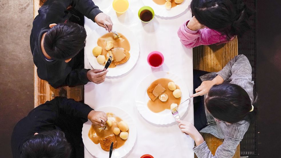 Kinder sitzen vor ihrem gemeinsamen Mittagessen. Auch in Aurich werden die Angebote zum kostenfreien Abendbrot beim Kinderschutzbund und im Familienzentrum dankend angenommen. Foto: DPA