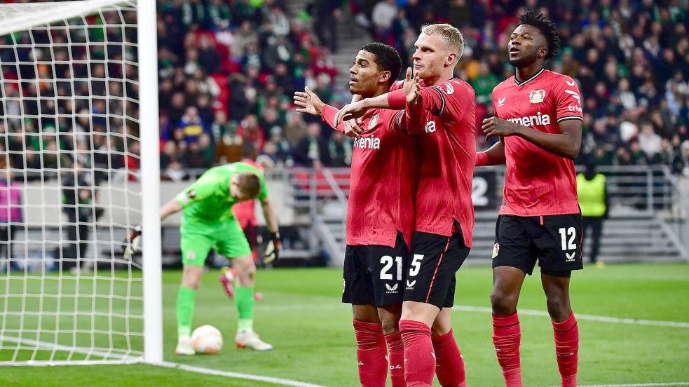 Leverkusens Torschütze Amine Adli (l-r) jubelt nach seinem Tor zum 0:2 mit Mitchel Bakker und Edmond Tapsoba. Foto: Marton Monus/dpa