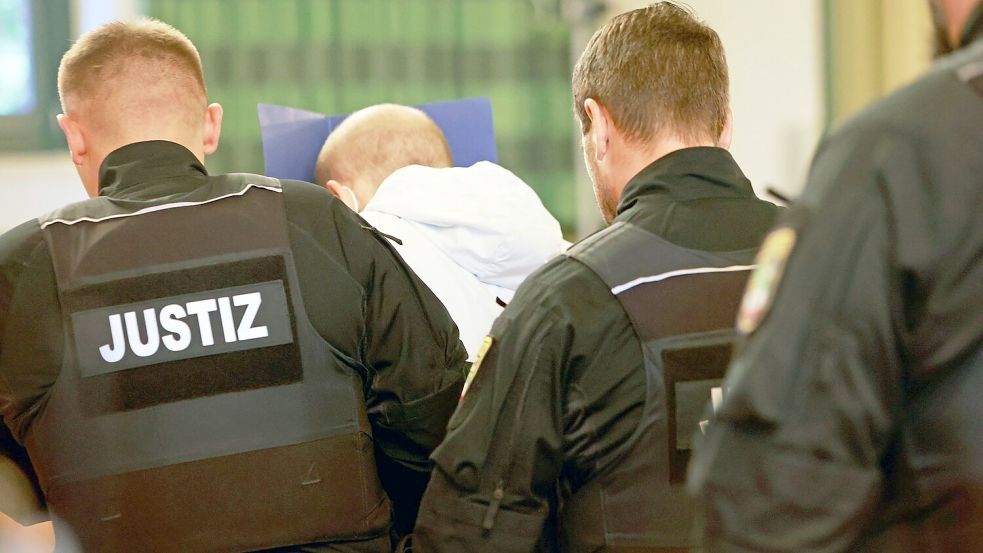 Der wegen Mordes angeklagte Mann (M) versteckt auf dem Weg in den Gerichtssaal sein Gesicht. Foto: Matthias Bein/dpa