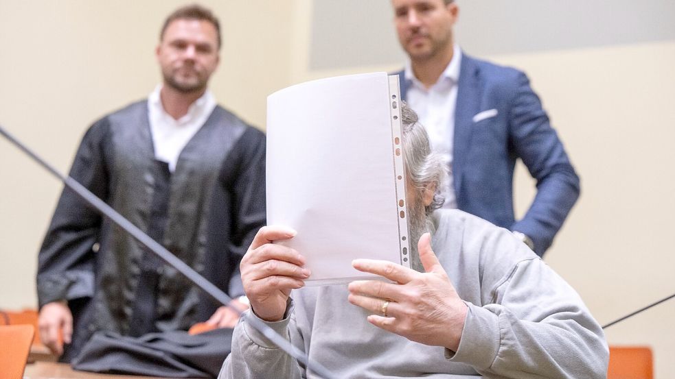 Der Angeklagte hält sich im Gerichtssaal ein Blatt Papier vor das Gesicht. Im Hintergrund stehen seine Anwälte. Foto: Peter Kneffel/dpa