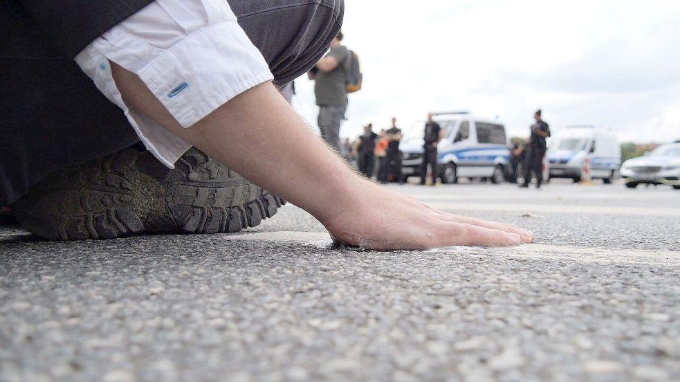 Ein Klimaaktivist hat sich mit der Handfläche am Asphalt einer Straße in der Bremer Innenstadt festgeklebt. Foto: Jörn Hünecke/dpa