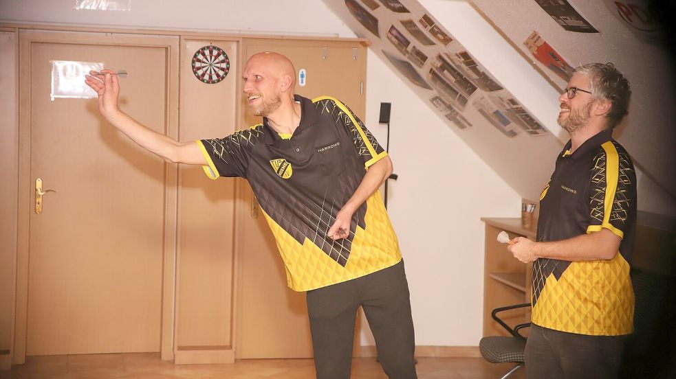 Henning Saathoff (rechts) beobachtet, wie Dirk Saathoff seine Pfeile während des Trainings im Vereinsheim des TuS Weene auf der Dartscheibe platziert. Dirk Saathoff, der den Spitznamen „Blitz“ trägt, gilt als ein nervenstarker Werfer. Einer, der ruhig bleibt, wenn es mal nicht rund läuft. Fotos: Wilfried Gronewold (2)/privat (1)