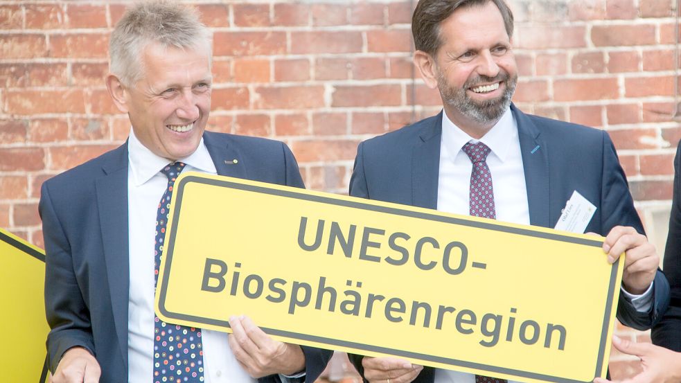 Peter Südbeck (links) ist der Leiter der Nationalparkverwaltung. Hier sitzt er neben Niedersachsens Umweltminister Olaf Lies (SPD). Sie halten ein Ortsschild mit dem Titel „Unesco-Biosphärenregion“. Foto: Lennart Stock/dpa